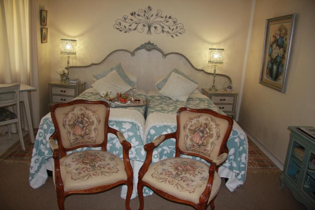 Un dormitori amb un llit, dues taules de nit, dues cadires, una commode i una decoració mural.