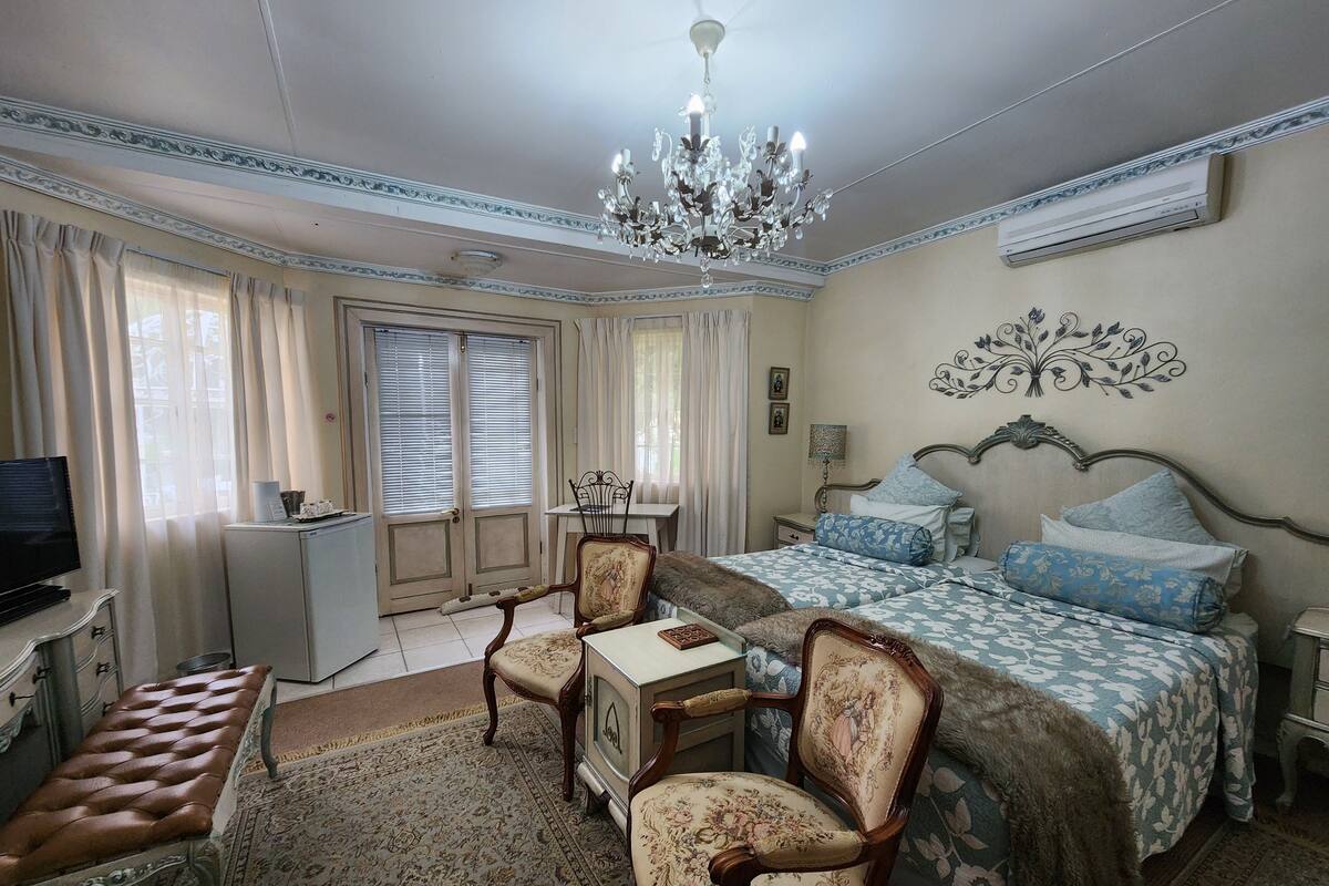 A bedroom with a bed, a desk, a chair, a television, and a chandelier.