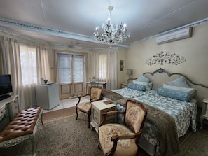 A bedroom with a bed, a desk, a chair, a television, and a chandelier. - THE SUMMER PLACE BOUTIQUE GUESTHOUSE (Bloemfontein)
