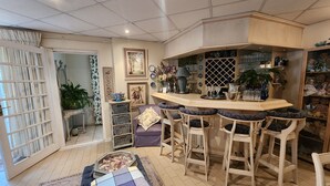 A bar area with a counter and stools, a dining area with a table and chairs, and a decorative wall with various items. - THE SUMMER PLACE BOUTIQUE GUESTHOUSE (Bloemfontein)