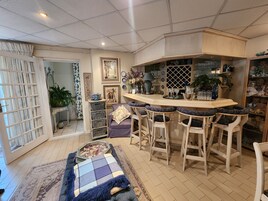 Una zona de bar con mostrador y taburetes, un comedor con mesa y sillas, y una pared decorativa con diversos objetos.