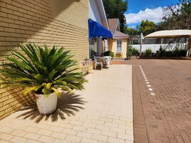 Un patio con una planta en maceta, una mesa con sillas y un edificio con toldo azul.