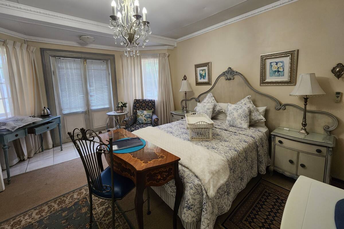 A bedroom with a bed, a desk, a chair, a chandelier, and two bedside tables with lamps.
