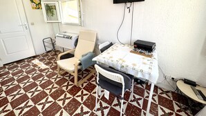 A room with a tiled floor, a chair, a table with a floral tablecloth, a wall-mounted TV, and a heater. - VIEUX NICE VISTA AP4503 by Riviera Holiday Homes (Niza)