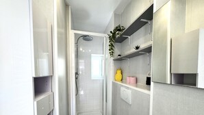 A modern bathroom with a shower, toilet, and shelves with toiletries. - VIEUX NICE VISTA AP4503 by Riviera Holiday Homes (Niza)