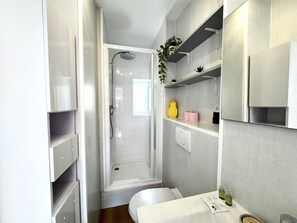 A modern bathroom with a shower, toilet, and shelves with toiletries. - VIEUX NICE VISTA AP4503 by Riviera Holiday Homes (Niza)