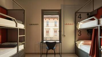 Une chambre de dortoir avec des lits superposés, un bureau et une fenêtre donnant sur un immeuble.