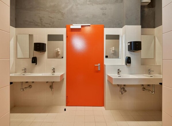 A restroom with two sinks, a mirror, a soap dispenser, and an orange door.