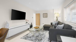 Ein modernes Wohnzimmer mit einem Flachbildfernseher, einem Glastisch, einem grauen Sofa und einem weißen Schrank.