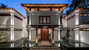 A two-story building with a central entrance, a wooden pergola, and a tiled floor leading to a door. - Azara is a serene luxury sanctuary in Goa designed for calm and escape. (Candolim)