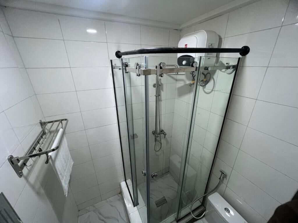 A glass-enclosed shower stall with a handheld showerhead, a towel rack, and a toilet.