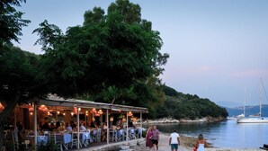 En udendørs restaurant med borde og stole, med udsigt over vand og et bakket landskab.