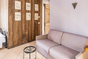 Una habitació amb una paret de fusta, un sofà beix, una taula rodona petita i dibuixos emmarcados a la paret.