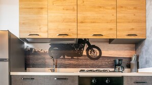 Une cuisine avec des meubles de rangement en bois, une cuisinière à gaz et un autocollant représentant une moto sur le pare-feu.