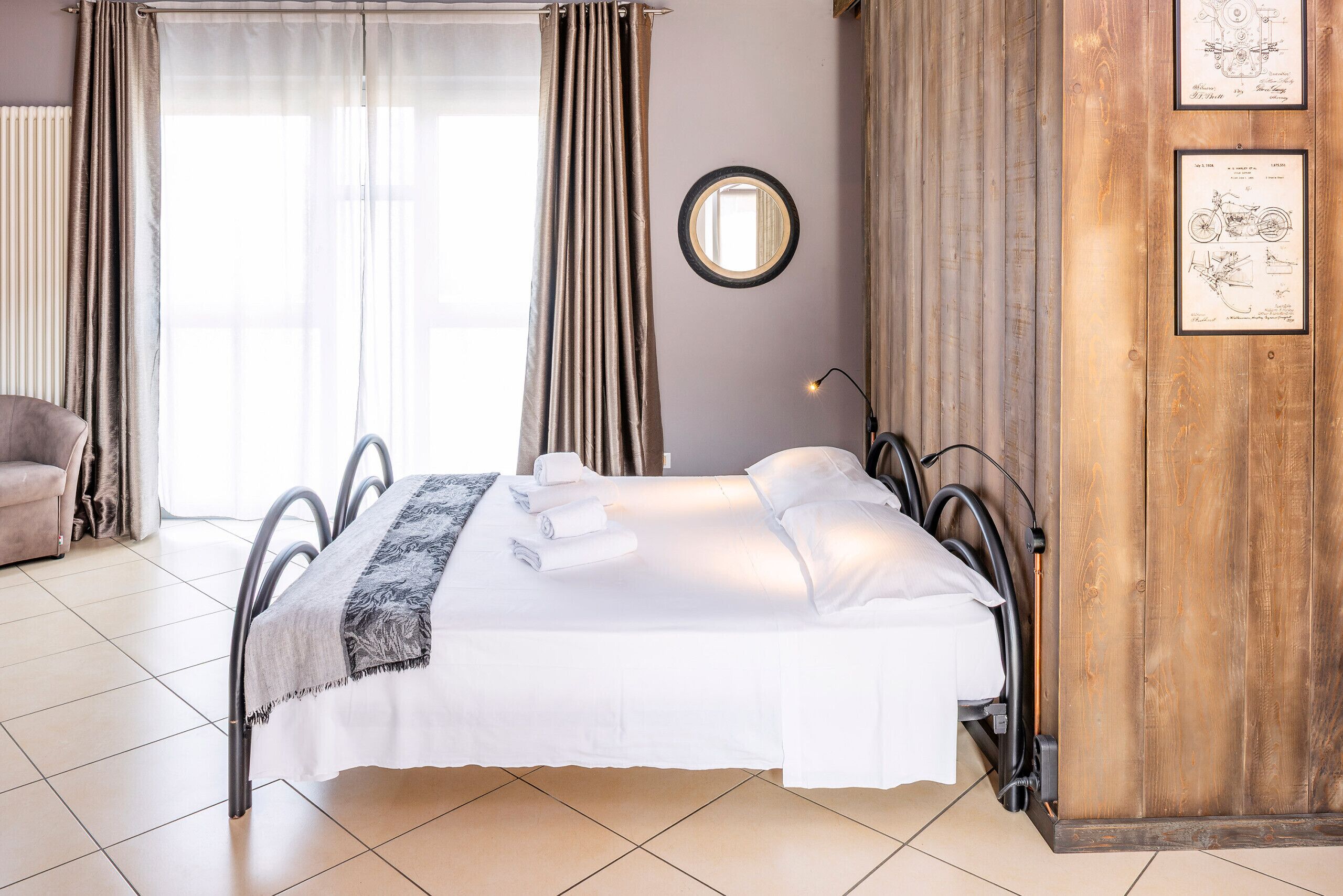 A neatly made bed with white linens, a grey throw, and a mirror on the wall.