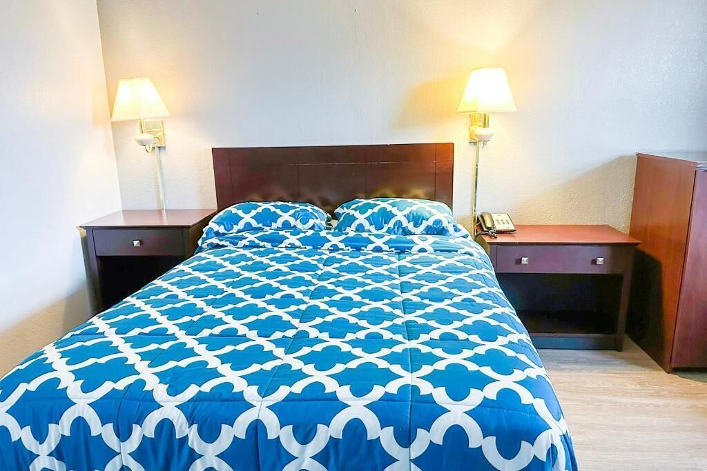 A hotel room with a bed, two bedside tables, a nightstand, and a lamp.