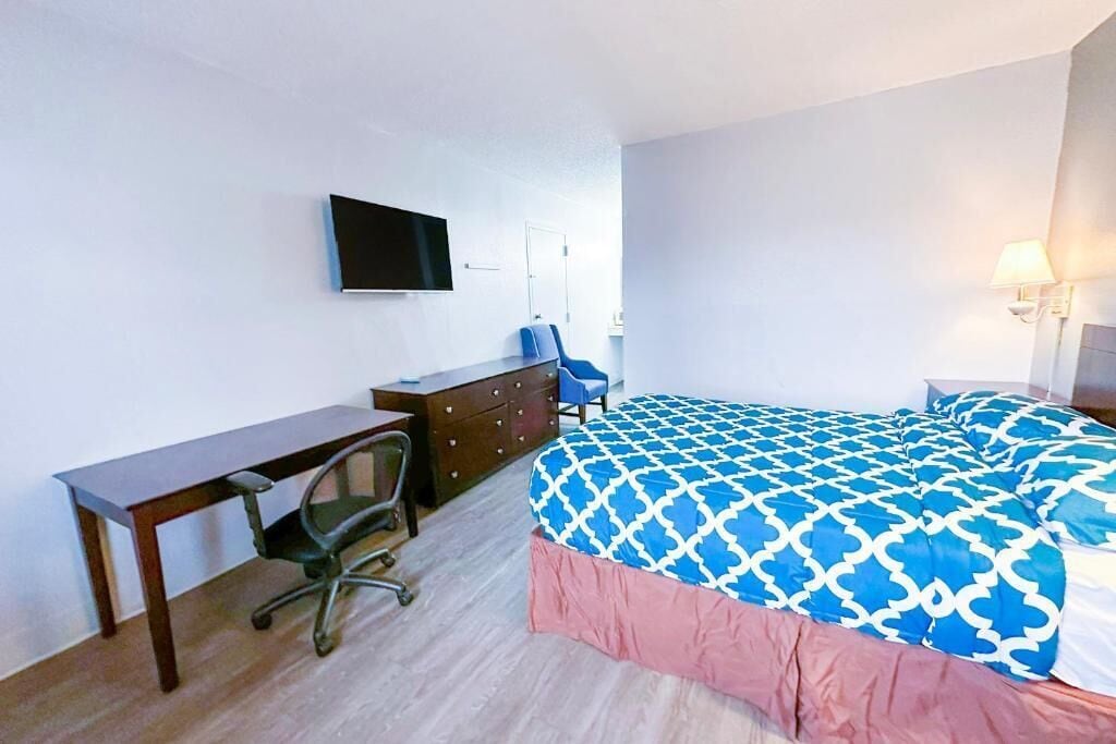 Hotellihuone, jossa on sänky, työpöytä, tuoli, televisio ja lamppu.