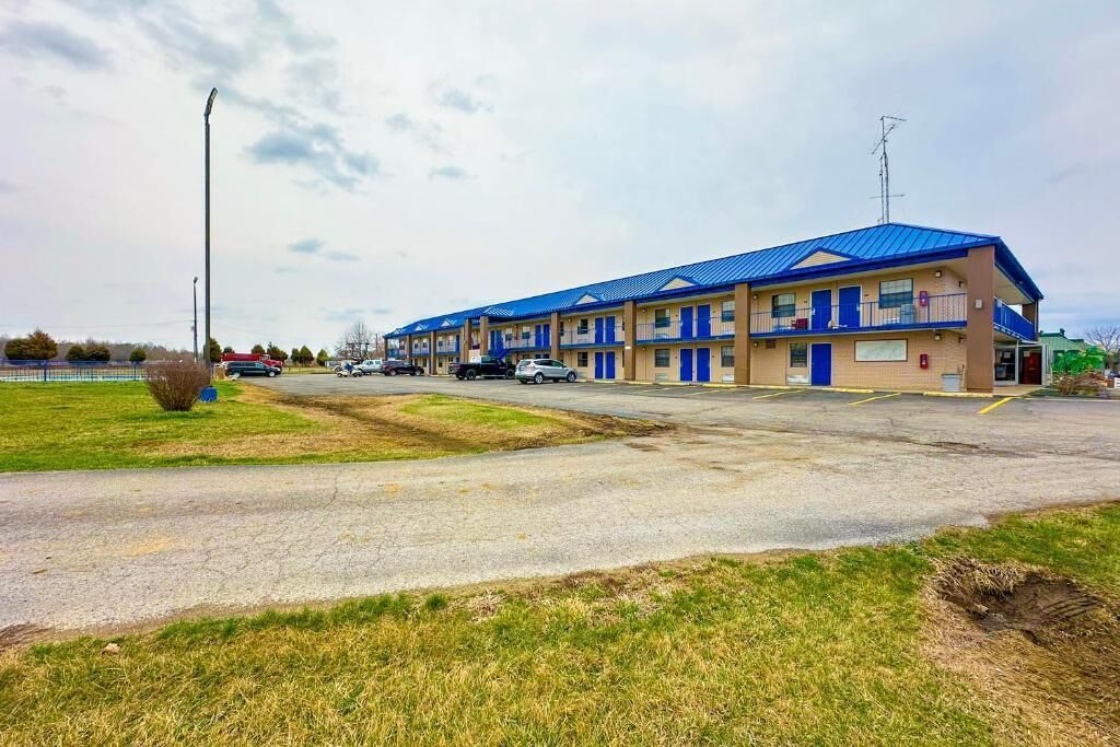 Motel amb teulada blava i parets beix, amb un pàrquing i una zona verda al davant.