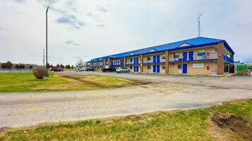 Motel amb teulada blava i parets beix, amb un pàrquing i una zona verda al davant.