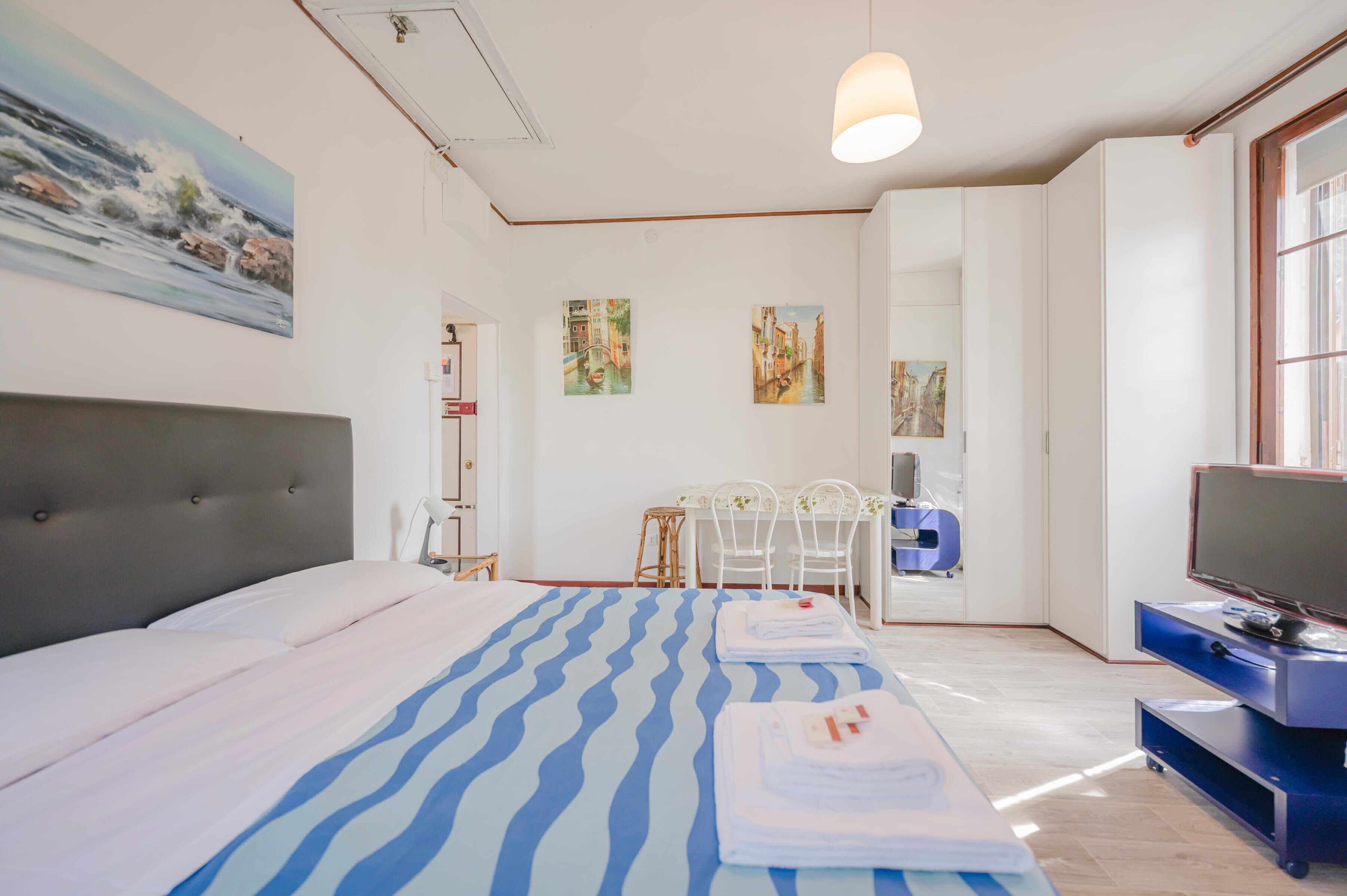 Una habitació d'hotel amb un llit, escriptori, televisió i obra d'art a les parets.
