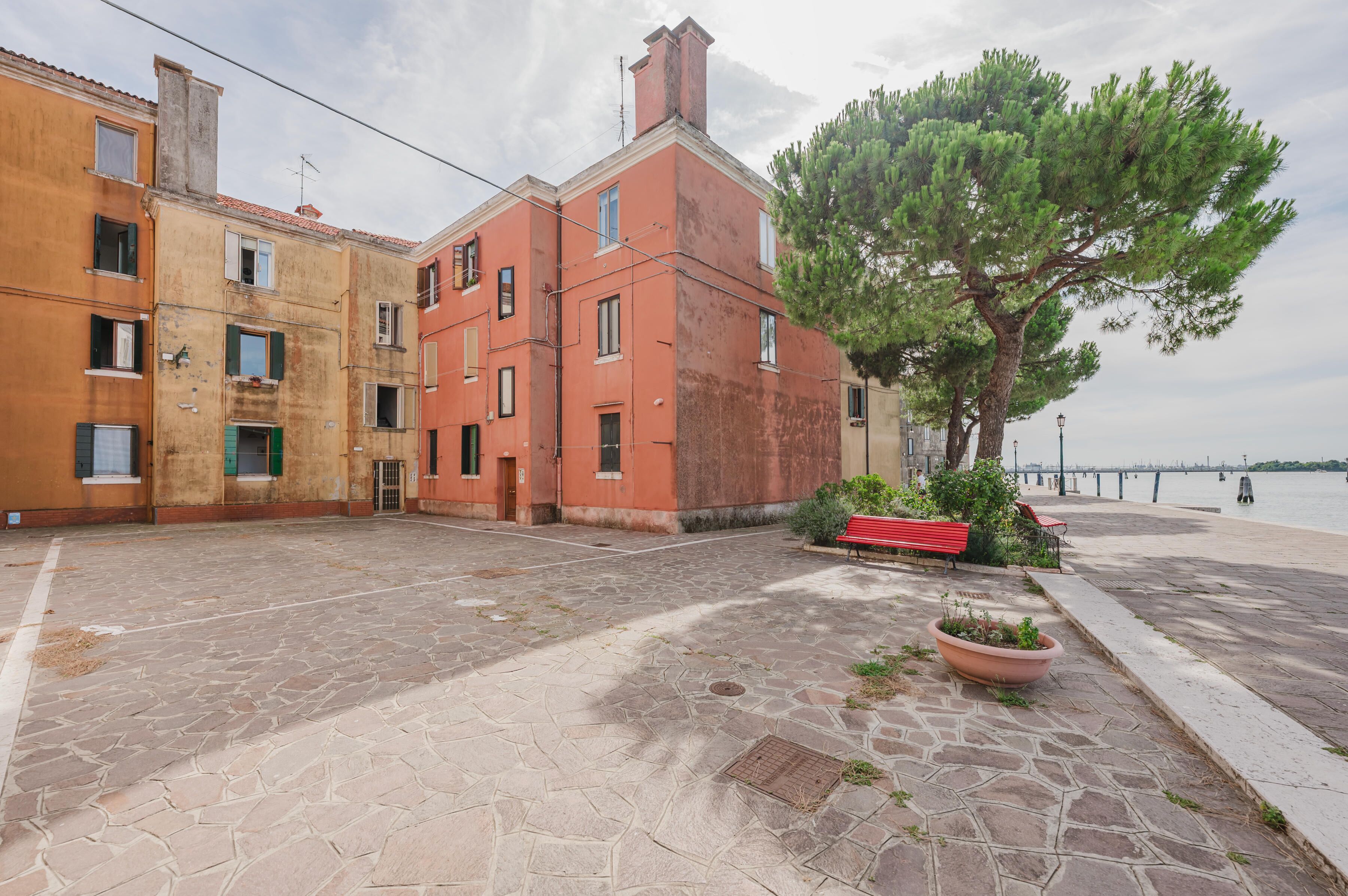 Un patio con pavimento de piedra, un banco rojo y un árbol.
