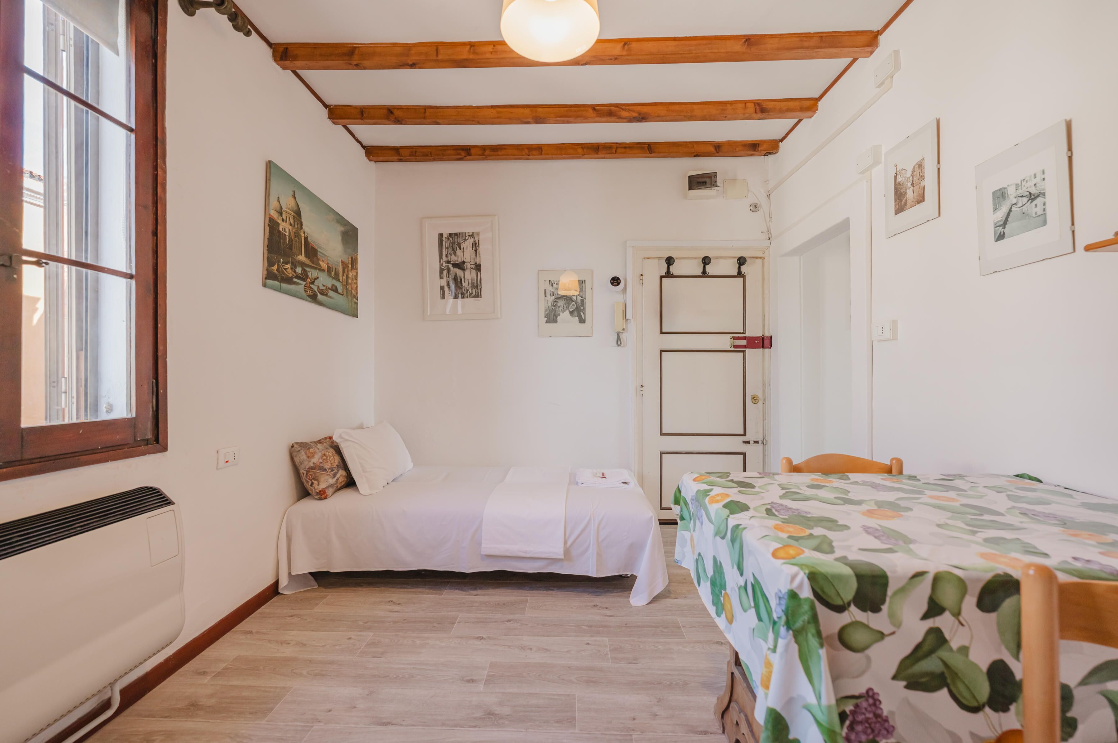 A room with a bed, a table with a tablecloth, a radiator, and a window.