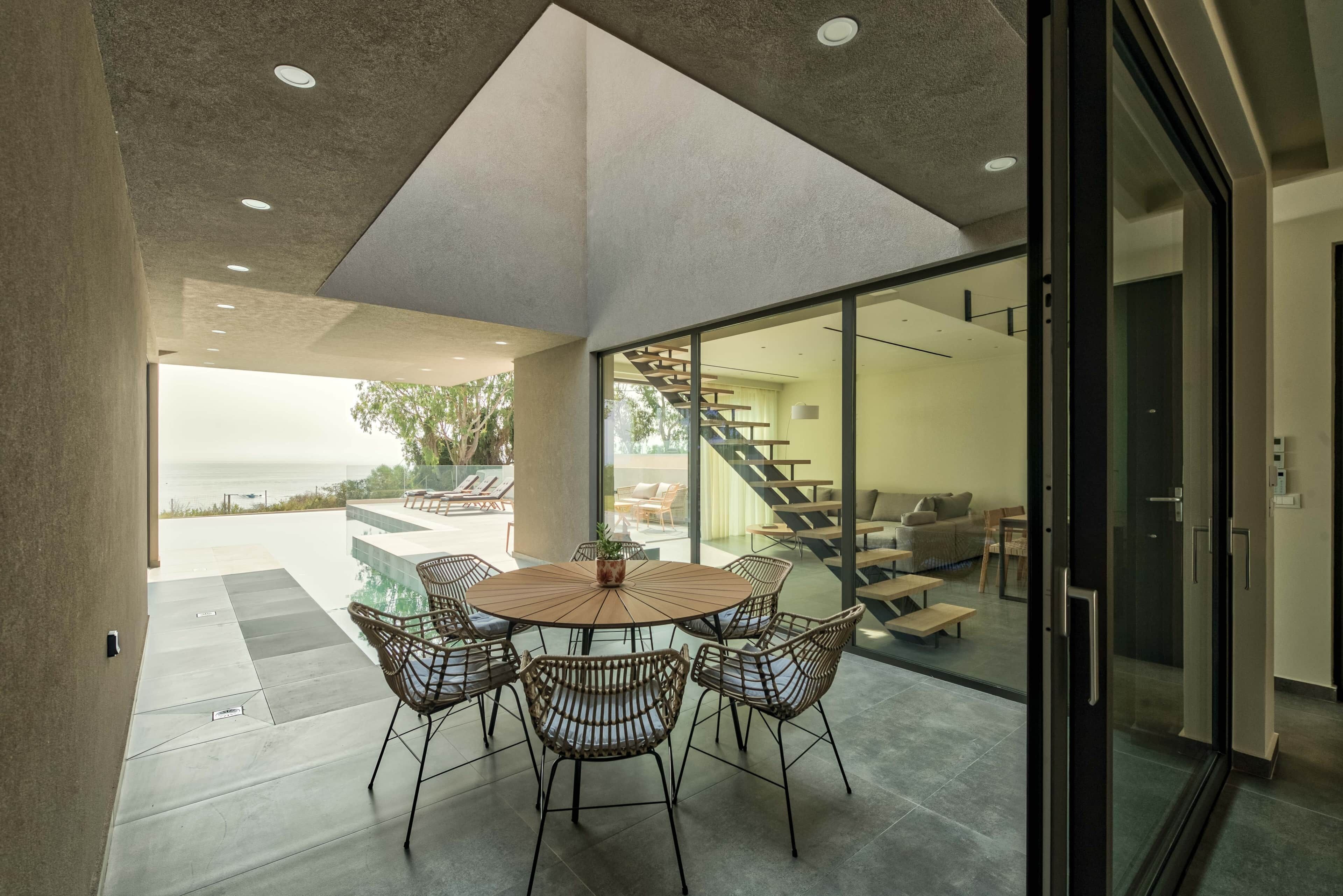 A modern dining area with a round table and wicker chairs, a staircase, and a view of the outdoors.