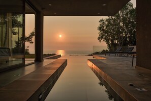 Ein moderner Poolbereich im Freien mit Liegestühlen und Blick auf den Sonnenuntergang über dem Wasser.