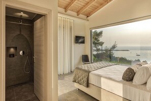 Ein Schlafzimmer mit großem Fenster, Dusche und Bett mit Meerblick.