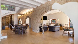 A spacious interior with a high ceiling, exposed brick arches, a dining area with a table and chairs, and a seating area with sofas and a coffee table. - Casa Vella Del Panta: Vacation Home with Sea Views, Private Pool, and Wi-Fi (Riudecanyes)