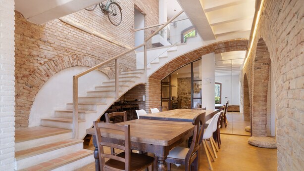 A spacious dining area with a long wooden table and chairs, a brick wall, and a staircase leading to an upper level. - Casa Vella Del Panta: Vacation Home with Sea Views, Private Pool, and Wi-Fi (Riudecanyes)