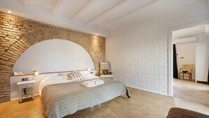 A bedroom with a brick wall, a large bed, a nightstand, a lamp, and a door leading to another room. - Casa Vella Del Panta: Vacation Home with Sea Views, Private Pool, and Wi-Fi (Riudecanyes)