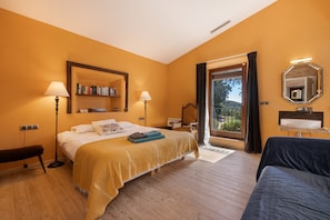 Ein Hotelzimmer mit Bett, Nachttischlampen, einer Bank, einem Bücherregal, einem Spiegel und Blick durch eine Glastür.