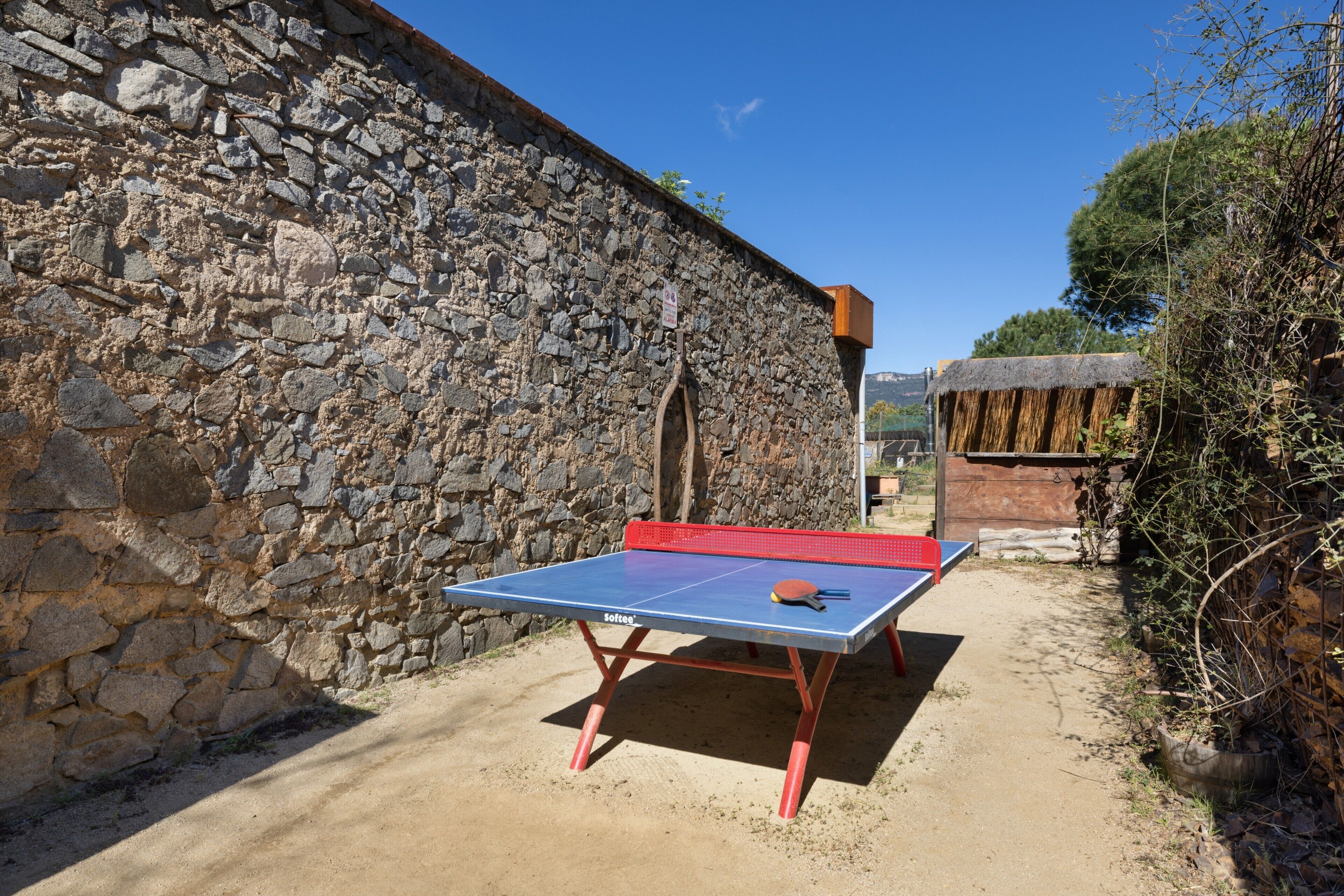 Mesa de tenis de mesa al aire libre con un muro de piedra y árboles al fondo.