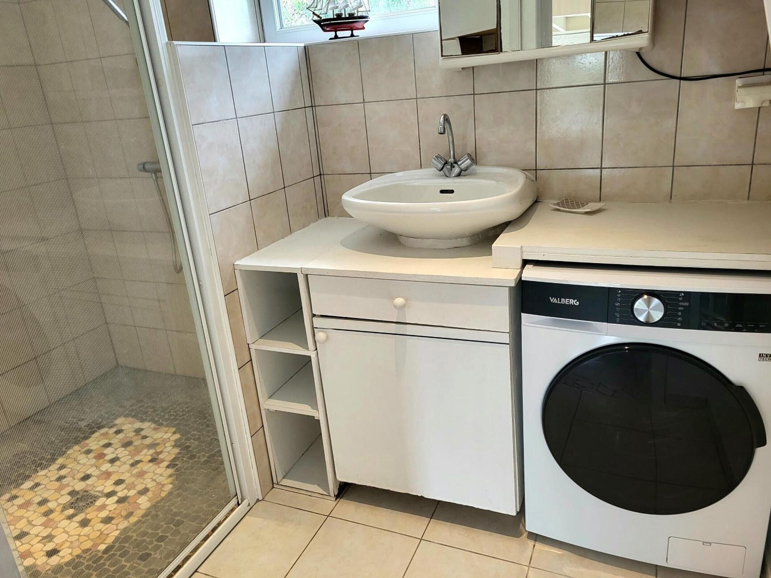 Ein kleines Badezimmer mit Waschbecken, Waschmaschine und einem kleinen Spiegel.