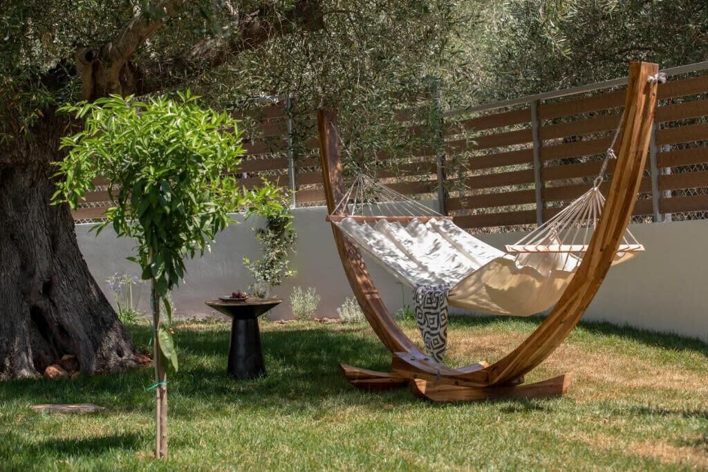 A hammock under a tree, a small table with a plant, and a wooden fence.