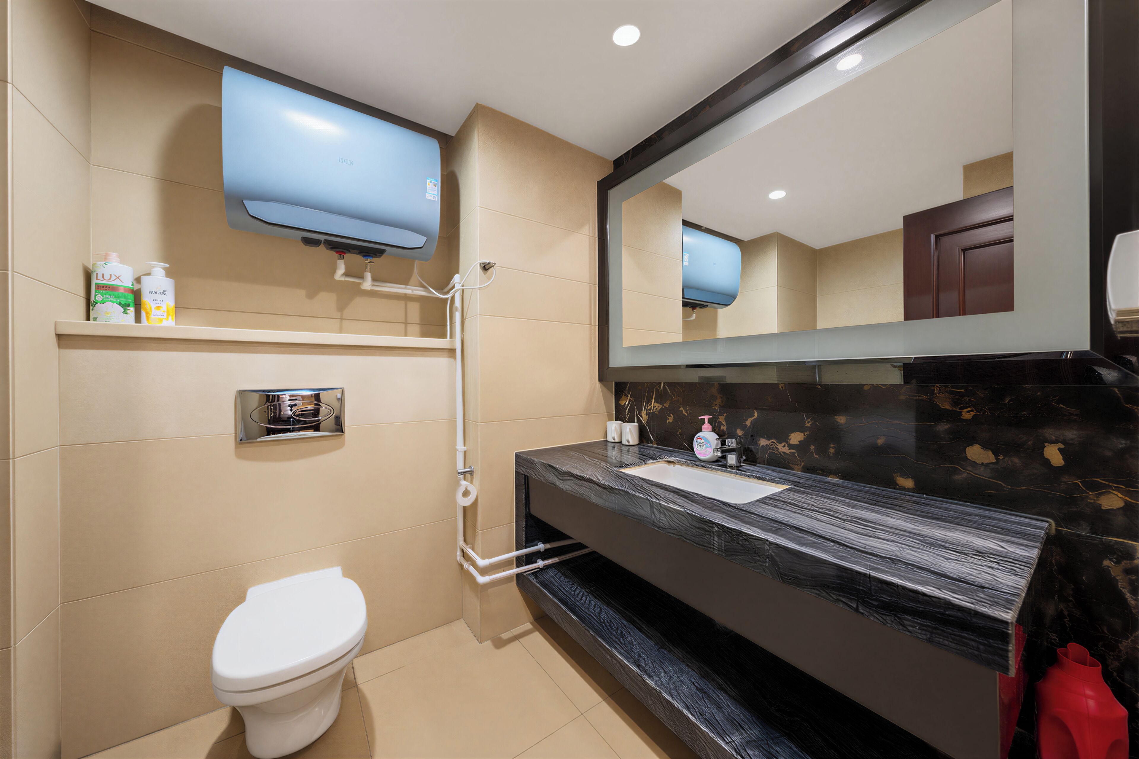 A modern bathroom with a toilet, a sink, a mirror, a television mounted above the sink, and a shelf with toiletries.