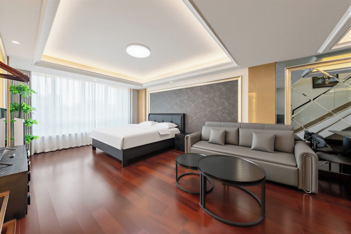 Una habitación de hotel moderna con cama, sofá, dos mesitas auxiliares, televisión y una escalera.