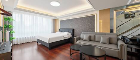 A modern hotel room with a bed, sofa, two side tables, a TV, and a staircase.