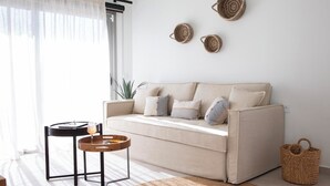 Un soggiorno con un divano color beige, un piccolo tavolino in legno con un vassoio, un cesto di vimini e una mensola a parete con cesti intrecciati.