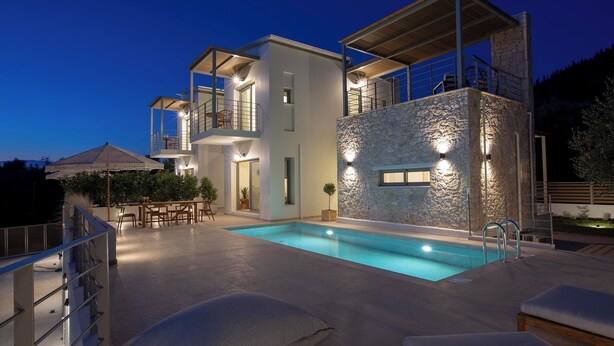 Una moderna casa a due piani con piscina, mobili da esterno e un muro in pietra.