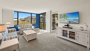 A living room with a TV, a sofa, a coffee table, and a cabinet with board games. - Loggerhead Cay 362: Updated Coastal Charm – Steps to Beach with Gulf Views & New (Sanibel)