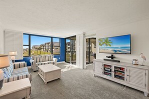 A living room with a TV, a sofa, a coffee table, and a cabinet with board games. - Loggerhead Cay 362: Updated Coastal Charm – Steps to Beach with Gulf Views & New (Sanibel)