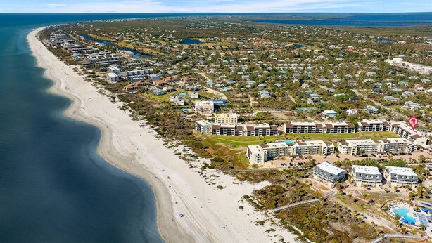An aerial view of a coastal resort area with beachfront properties, a central cluster of buildings, and a marked location pin. - Loggerhead Cay 362: Updated Coastal Charm – Steps to Beach with Gulf Views & New (Sanibel)