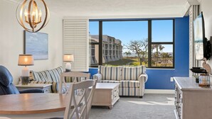 A room with a large window, striped sofas, a dining table, and a chandelier. - Loggerhead Cay 362: Updated Coastal Charm – Steps to Beach with Gulf Views & New (Sanibel)
