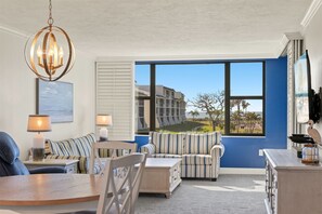 A room with a large window, striped sofas, a dining table, and a chandelier. - Loggerhead Cay 362: Updated Coastal Charm – Steps to Beach with Gulf Views & New (Sanibel)