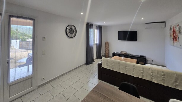 A modern living room with a large window, a flat-screen TV, a clock, and a dining area with a table and chairs. - U Miu Sognu by Pinarello Villa Services (Sainte-Lucie de Porto-Vecchio)