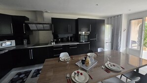 A modern kitchen with dark cabinets, a dining table set for four, and a large window. - U Miu Sognu by Pinarello Villa Services (Sainte-Lucie de Porto-Vecchio)