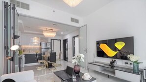 A modern living room with a dining area, a kitchen in the background, and a large flat-screen TV mounted on the wall. - Vogue | Pearlz by Danube near Ibn Battuta Mall (Dubai)
