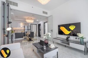 A modern living room with a dining area, a kitchen in the background, and a large flat-screen TV mounted on the wall. - Vogue | Pearlz by Danube near Ibn Battuta Mall (Dubai)